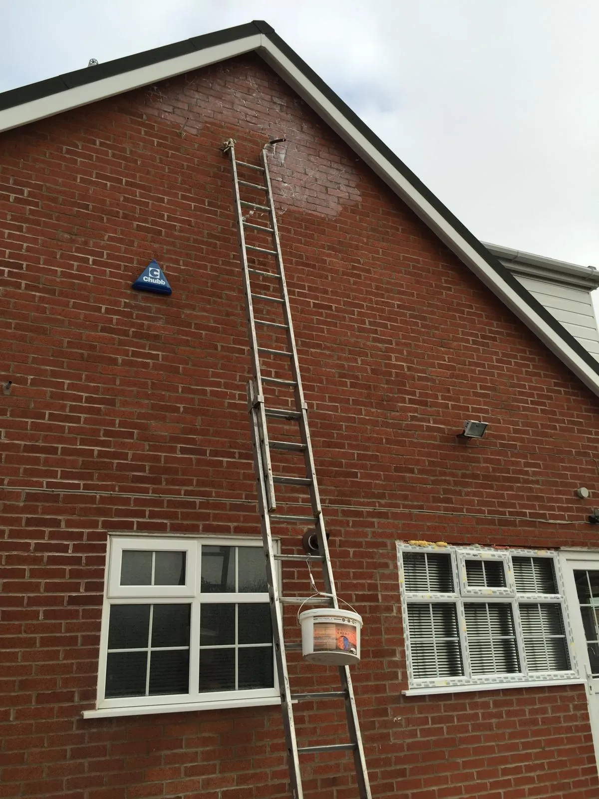 Ladder against a red brick gable with a tub of Masonry Crème hooked on a rung