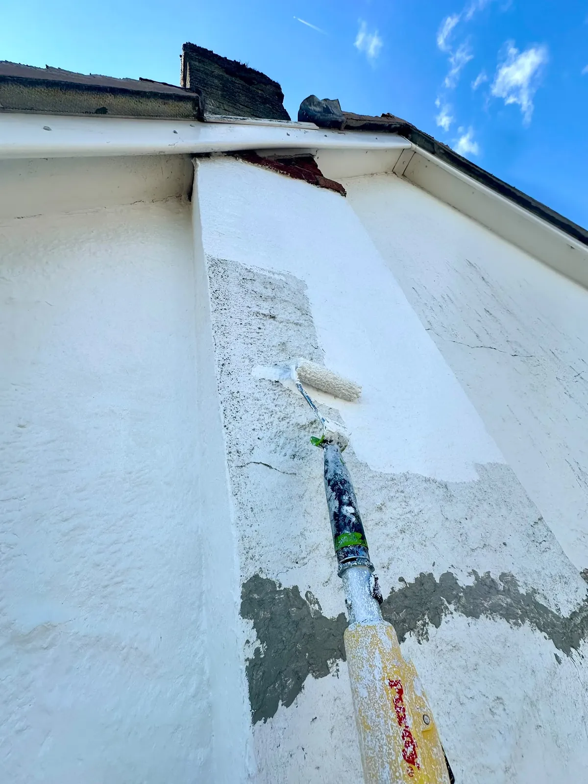 Masonry coating being rolled over a repaired section of gable