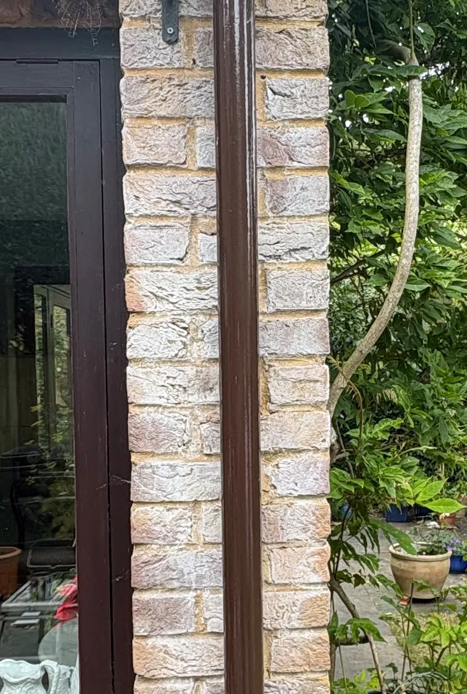 Buff brick pier with heavy white salt bloom following the wet line beside a cast iron downpipe